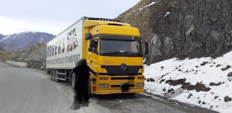 Yellow truck with refrigerated trailer parked on a snowy mountain road